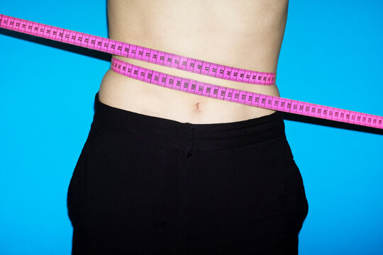 Pink measurement tape around waist against blue background