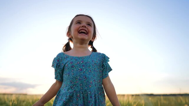 A girl runs joyfully across a field, with laughter on her face. The girl wears a blue dress, enjoying the open space and the warm light of the sunset.