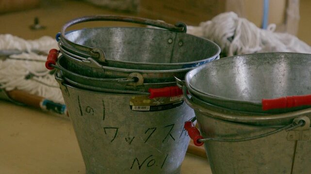 Galvanized metal buckets and discarded mops sit inside an abandoned room.