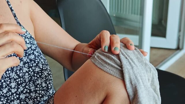 Close up of a woman's hands meticulously sewing fabric with a needle and thread, showcasing the traditional skill of hand stitching and repairing clothes in a home environment