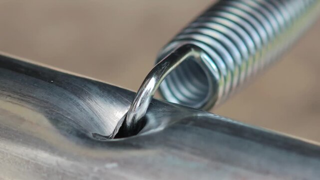Close up of a galvanized steel spring hooked to a metal frame, highlighting tension, elasticity, and mechanical connection as the coil stretches and rebounds under load
