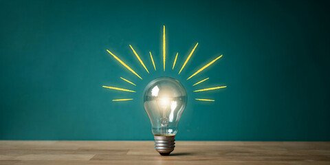 glowing light bulb with bright rays shining outwards symbolizing a new idea or innovation on a teal background. © kobita Art