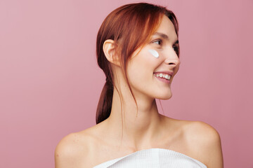 Smiling woman profile portrait applying face cream on pink background. Skincare and beauty care concept. Soft studio lighting creates a happy and clean aesthetic layout for wellness. © SHOTPRIME STUDIO