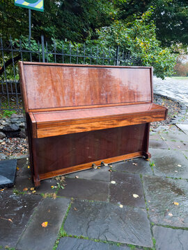 Old upright piano outdoor street abandoned wooden brown stone pavement autumn leaves vintage musical instrument fence city nostalgia