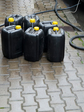 Black plastic canisters yellow caps wet paving tiles hose outdoor fuel storage containers industrial liquid water barrels group