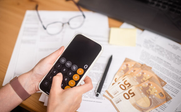 A calculator in female hands against a background of documents and money, creating the atmosphere of business and financial strategy. 