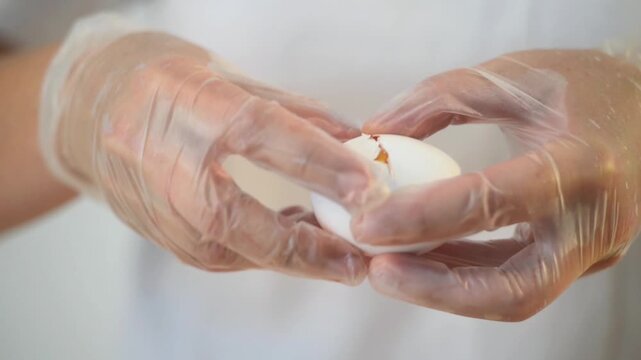 Chef in white uniform and gloves cracking a fresh egg with knife