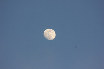The bright full moon hangs in the clear blue daytime sky © Mateusz
