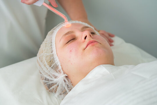 At a beauty salon, a focused care session includes darsonval treatment, a young woman, high frequency facial, a glass electrode, an esthetician, and facial skincare