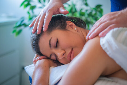 A serene young woman resting on a massage table with her eyes closed, experiencing a deeply relaxing shoulder massage from a professional therapist in a beauty salon, featuring therapeutic massage