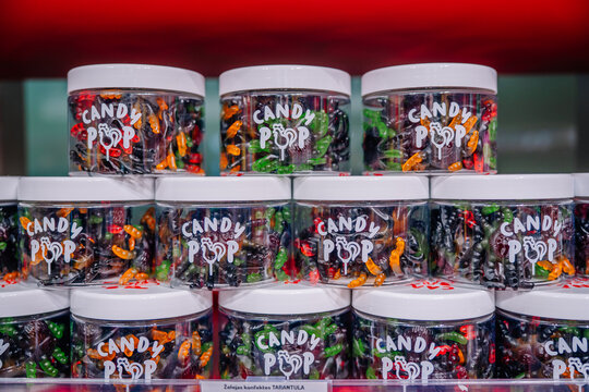 Colorful candy jars with assorted sweets and white lids arranged on retail shelves, featuring transparent containers and candy pop labels in a confectionery display