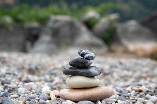 Stacked smooth stones on pebble beach with blurred water and duck in background, closeup with shallow depth of field
