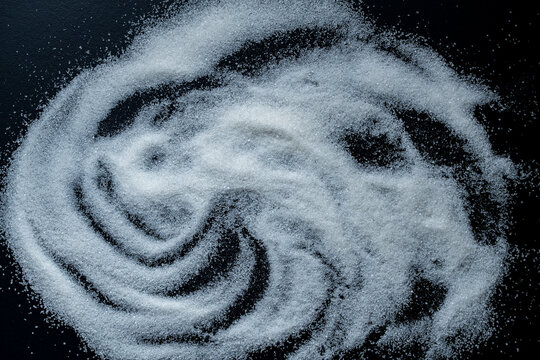 Spilled white sugar abstract swirl pattern on black background. White sugar crystals scattered in wave lines on dark desk. Creative backdrop for sweet life, food art, diabetes or cooking concept
