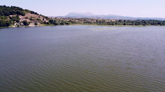 Beautiful aerial footage flying over a large tranquil lake. The green water has gentle ripples and the distant shore shows a village and Rtanj mountain in Serbia