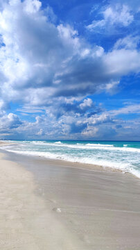 Beach shoreline with gentle waves under dramatic cumulus clouds and blue sky