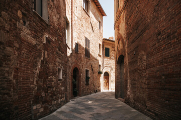Naklejka premium Empty narrow medieval street in the historic center of Montepulciano, Tuscany, Italy. Traditional brick and stone buildings along a picturesque old alley with sunlight and shadows.