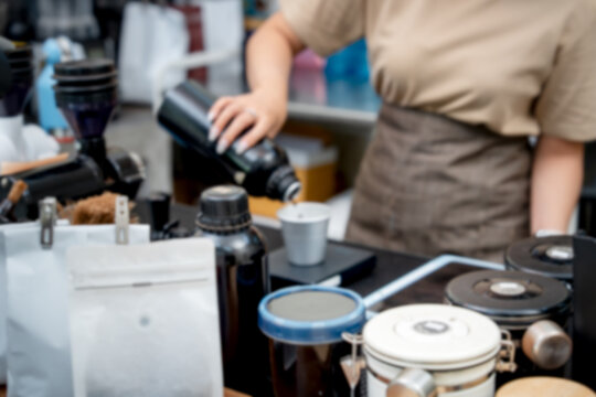 Blurred coffee shop background featuring a barista working with bottles and brewing equipment at a counter.
