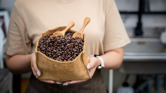  A person presents a burlap sack brimming with roasted coffee beans and wooden spoons at a caf&eacute;.
