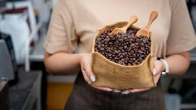 Detailed view of hands holding a burlap bag filled with roasted coffee beans and wooden spoons.