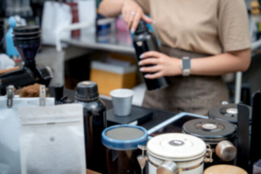Blurred coffee shop background featuring a barista working with bottles and brewing equipment at a counter.