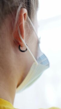 A girl with a braided hairstyle wears a face mask and an earring. The girl's face is partially visible from the back, showcasing the mask and earrings in the scene.