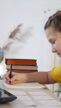 A girl sits at a table writing notes. The girl focuses on her work, surrounded by books and stationery, with a globe in the background.