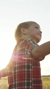 A boy stands against a sunny background, pointing towards the sky. The boy&rsquo;s plaid shirt catches the light, creating a bright atmosphere around him.