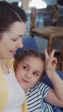 A woman and a girl are sitting together on a sofa. The girl playfully makes a gesture while talking to the woman, creating a moment of connection.