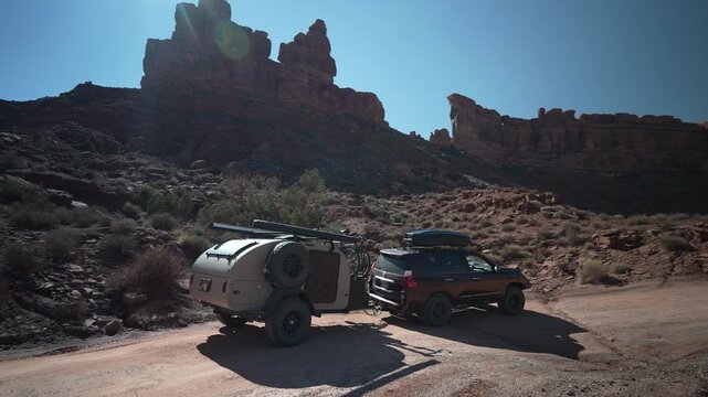 Traveling the rugged beauty of the Valley of the Gods in Utah, an SUV tows a teardrop camper trailer through breathtaking landscapes.
