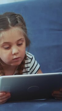 A girl sits focused on a tablet, engaging with the screen. The girl appears concentrated as she explores content on the tablet in a relaxed setting.
