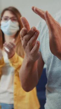 A man and a woman are clapping their hands in an indoor setting. Both individuals are wearing masks while expressing their applause in a supportive atmosphere.