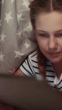 A girl is lying on a bed, focused on a tablet. The girl appears engaged while surrounded by a star-patterned blanket.