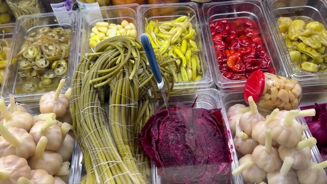 Assorted pickled vegetables including garlic cloves red cabbage and green beans are displayed indoors on a market counter. Traditional snacks, fermented food, grocery assortment.