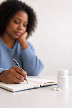 Woman writing in a journal beside medication for depression treatment. Mental health care and antidepressant use. Personal wellness, therapy and recovery concept. Copy space