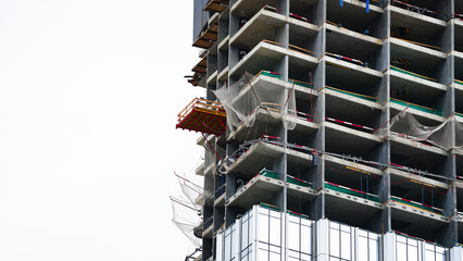 Unfinished high rise building with exposed concrete floors, safety netting and facade panels, showing construction progress, worker protection and modern building development © belavinstock