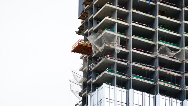 Unfinished high rise building with exposed concrete floors, safety netting and facade panels, showing construction progress, worker protection and modern building development