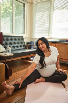 Native American expecting mother stretches in yoga pose in sun room