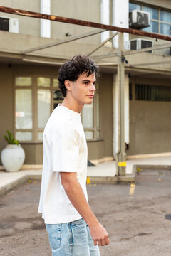 Man in a white t-shirt and denim shorts walking along a courtyard wall, looking straight ahead