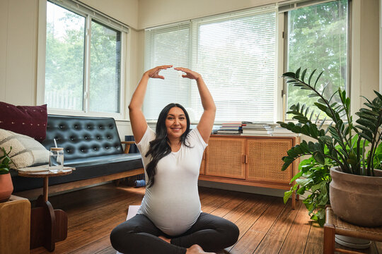 Native American expectant mother stretches in sun room during yoga practice