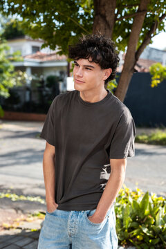 Confident man in a dark t-shirt with a slight smile standing beside a tree trunk on a quiet street