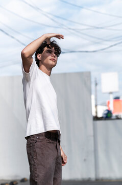 Man in a white t-shirt looking up with his hand raised above his forehead beneath power lines