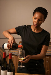 Fototapeta premium Hospitality and wine tasting, woman sommelier pouring white wine into a glass in a winery cellar for luxury lifestyle and gourmet dining experience