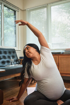 Native American expectant mother stretches during yoga in sun room