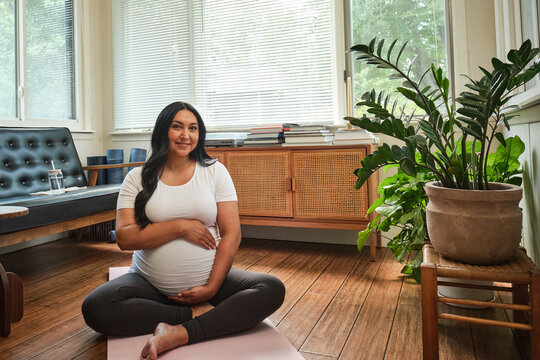 Native American expectant mother practices yoga in sun room while pregnant