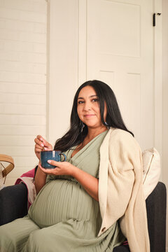 Native American pregnant woman smiling in a cozy space holding a bowl