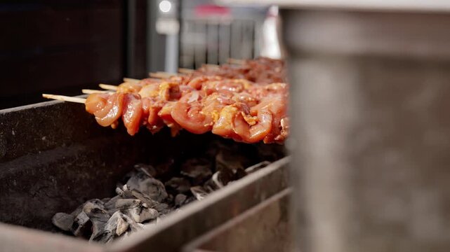 Rows of chicken skewers grill above charcoal in food market. Juicy marinated pieces roast over glowing coals, presenting freshly prepared street food with warm, savory appeal as heat cooks each piece.
