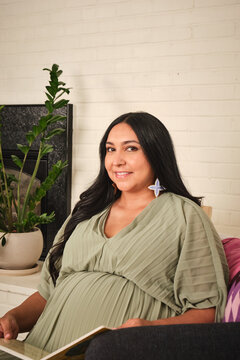 Pregnant Native American woman sits comfortably and reads in a home setting