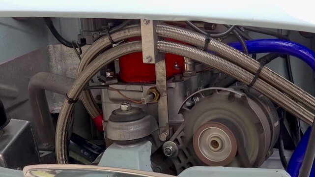 Running vintage car engine with rotating alternator pulley and braided steel hoses close up in detail.
