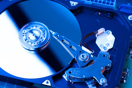 Inside an opened computer hard disk drive with illuminated blue neon lighting highlighting the platter and arm