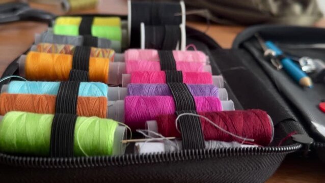 Colorful spools of thread arranged in an open sewing kit with scissors and crafting tools on a wooden table, close up view of sewing supplies